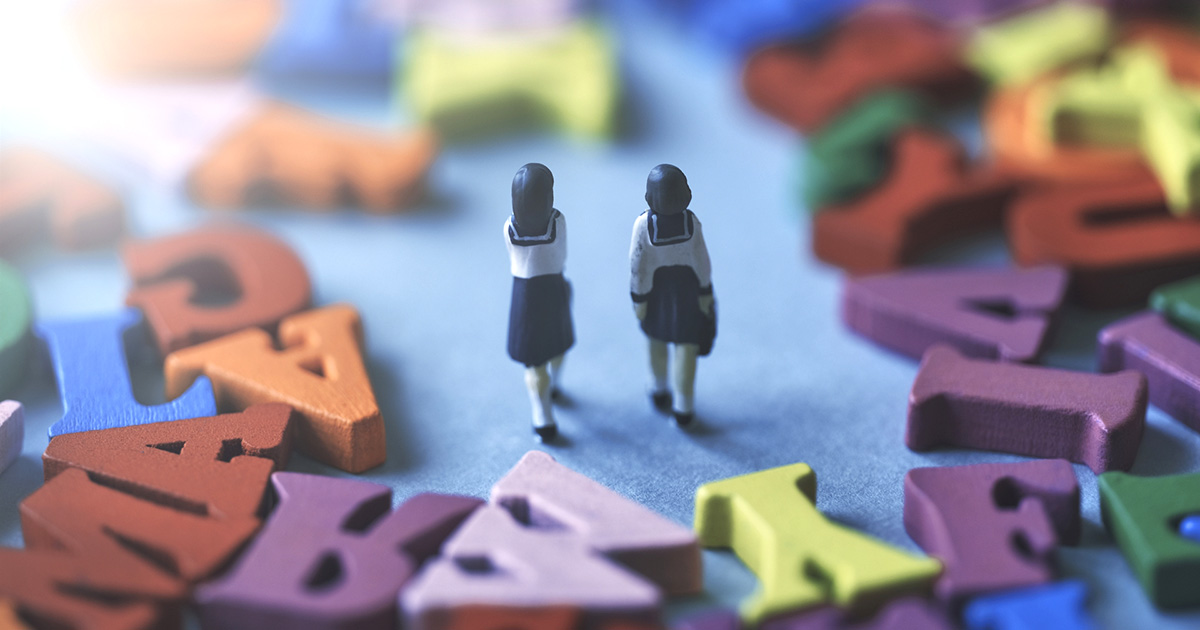 アルファベットの上を歩くセーラー服の学生二人